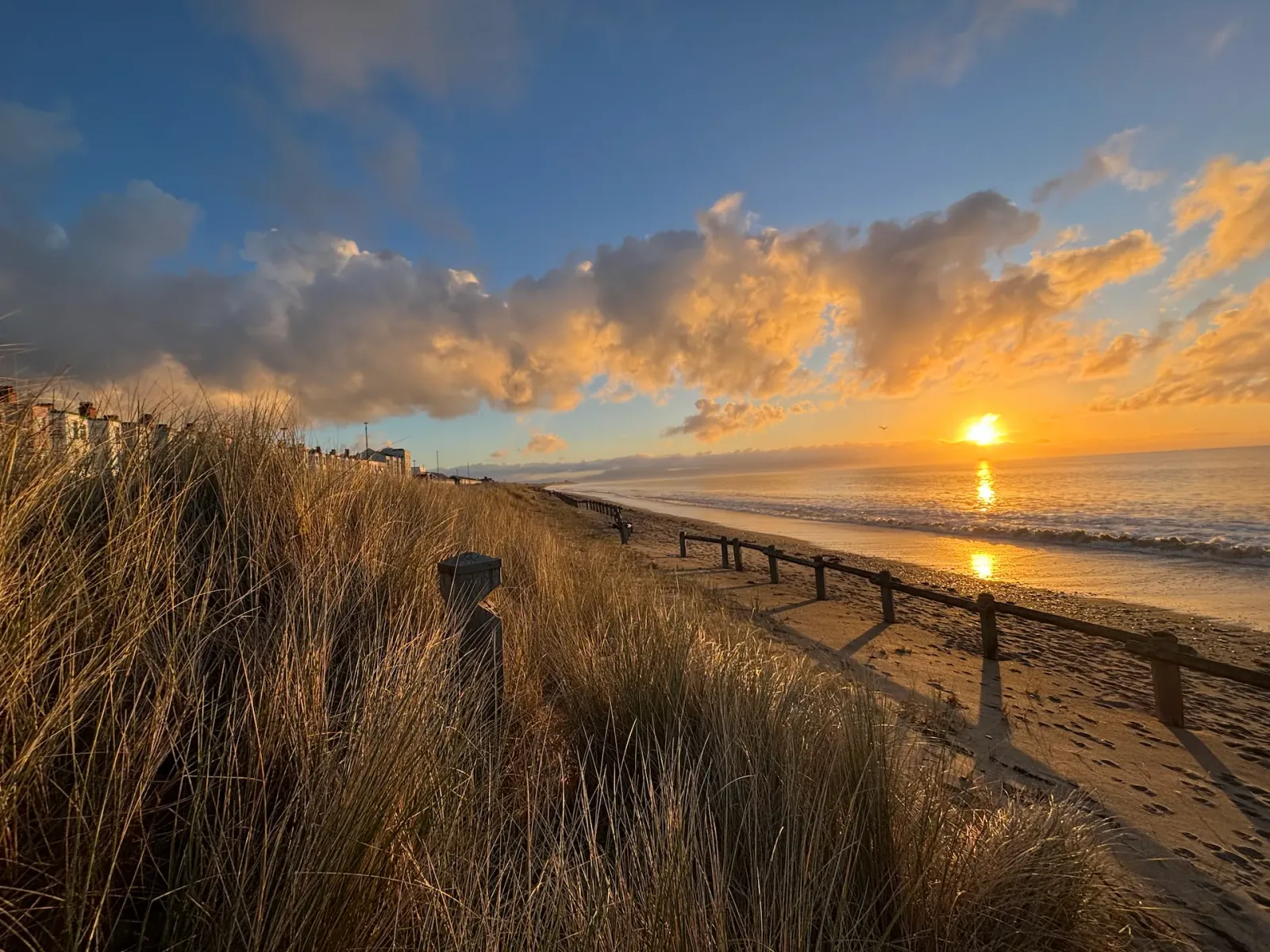 Sunset over the dunes, a wooden fence along the sand and the sun reflected in the sea